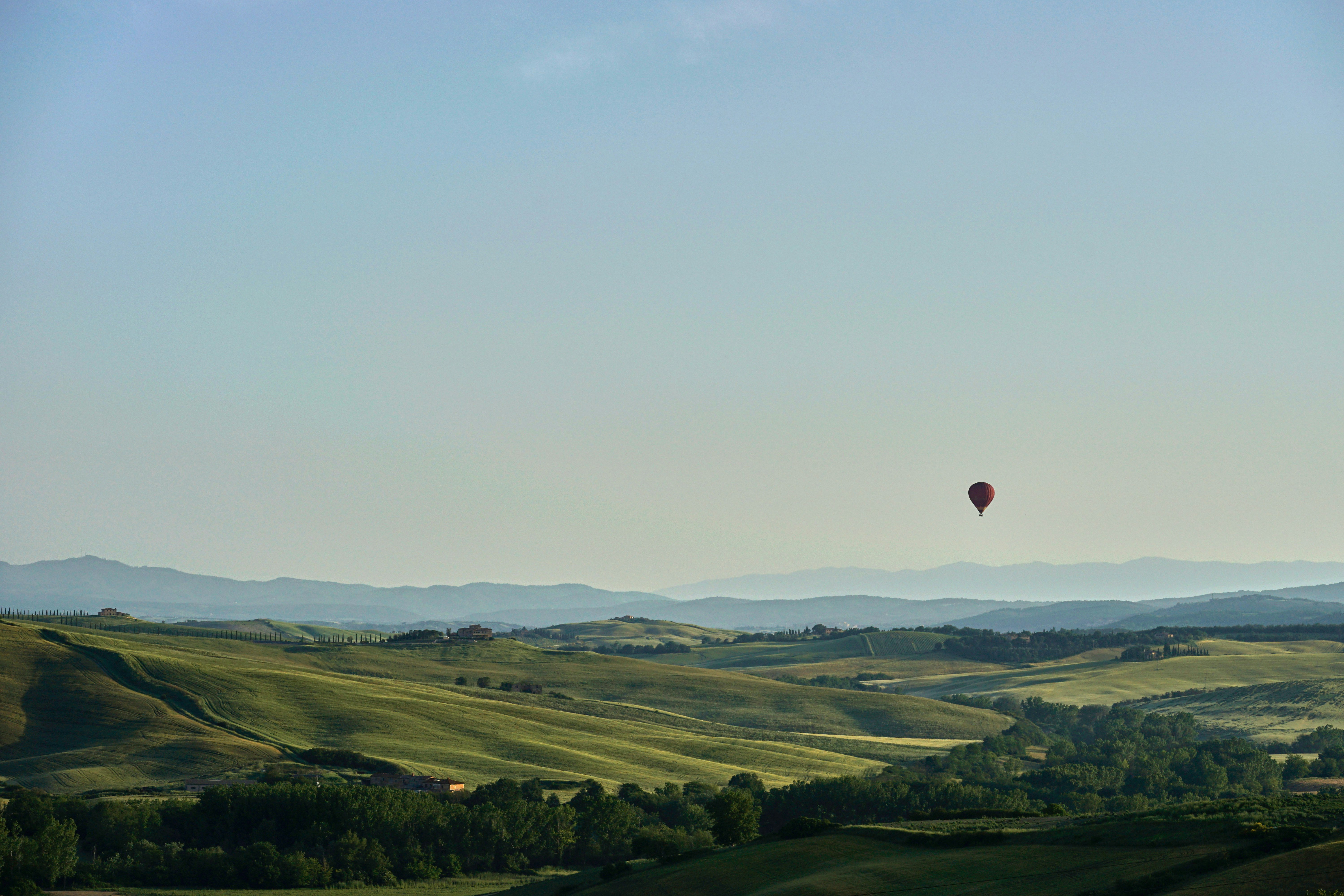 red hot air balloon flying over green grass field during daytime